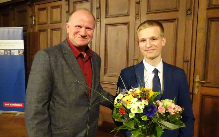 Ausbildungsmeister Steffen Papke und Philipp Szor bei der offiziellen Ehrung. Philipp Szor hält einen Blumenstrauß in der Hand und wurde für seinen herausragenden Ausbildungsabschluss ausgezeichnet.