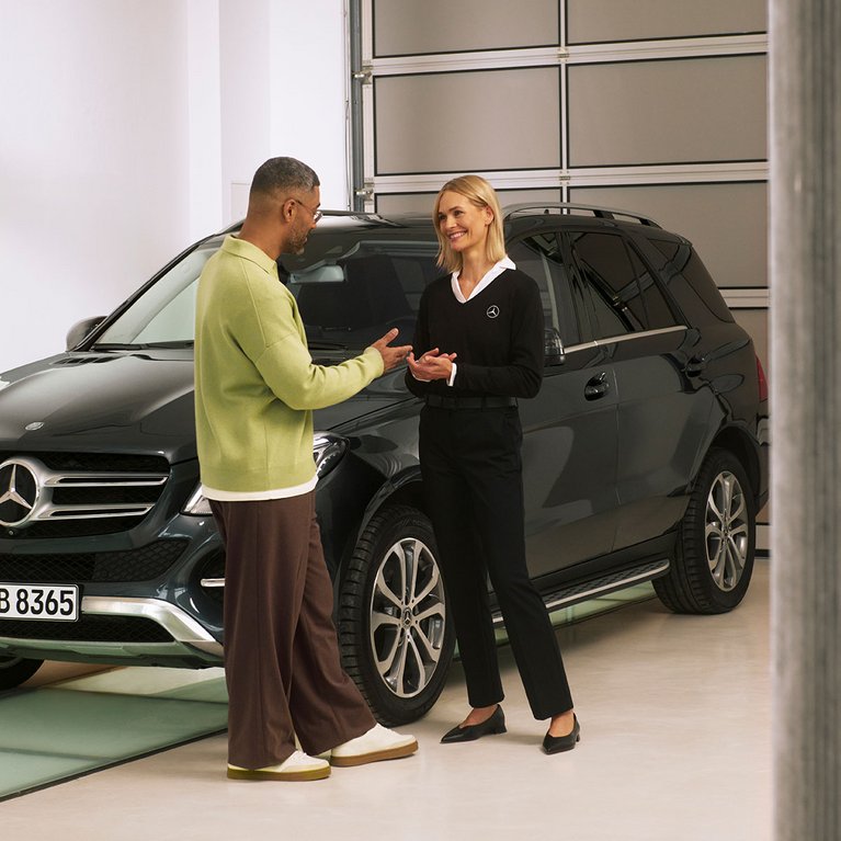 Ein Mercedes-Benz Kunde im Gespräch mit einer Serviceberaterin vor einem schwarzen SUV – Szene im Rahmen des Service VorteilsProgramms.