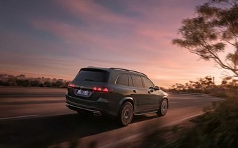Dunkler Mercedes-Benz GLS fährt bei Sonnenuntergang auf einer Straße. Die Heckansicht zeigt das elegante Design, die markanten Rückleuchten und die souveräne Präsenz des Premium-SUV.