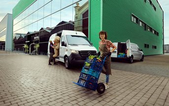 Promotionbild für die Vermietung eines Mercedes-Benz Transporter. Auf dem Foto ist zu sehen ein Mercedes-Benz Transporter der von einem Mann beladen wird. Rechts davon steht ein Mercedes-Benz Sprinter mit geöffneter Tür. Eine Frau entlädt den befüllten Mercedes-Benz Sprinter. Die Fahrzeuge stehen vor einem Hotel.