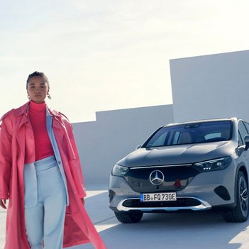 Eine Frau im stylischen pinken Mantel steht vor einem modernen Mercedes-Benz EQC, geparkt in minimalistischer Architektur. Symbol für Lifestyle, Eleganz und die flexible Mietoption Mercedes-Benz Rent PKW bei S&G.