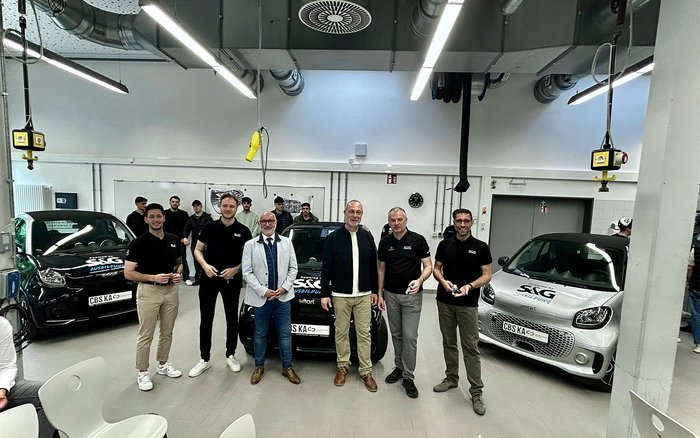 Gruppenfoto in einer Werkstatthalle: Mitarbeitende der S&G Automobil AG und Lehrkräfte der Carl-Benz-Schule Karlsruhe stehen gemeinsam vor vier vollelektrischen smart Fahrzeugen mit S&G-Beschriftung. Die Schlüsselübergabe markiert ein neues Kapitel der Ausbildungskooperation im Bereich Hochvolttechnologie.