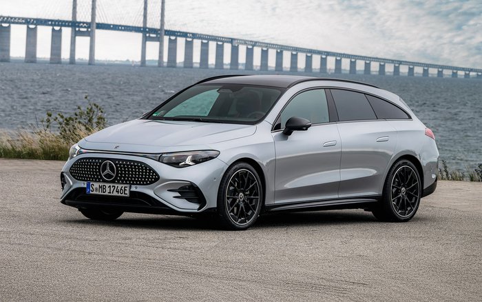 Seitenansicht eines silbernen Mercedes-Benz CLA Shooting Brake mit EQ Technologie mit schwarzem Dach, sportlichem Design und markanter Front, geparkt vor einer Küstenkulisse mit Brücke im Hintergrund.