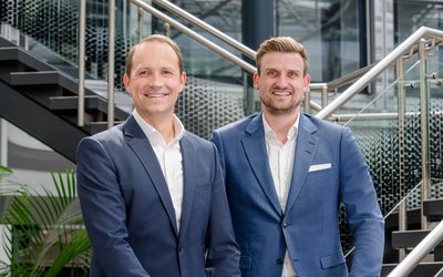 Daniel Daufer (links), CFO, und Christian Ullrich (rechts), neuer CEO der S&G Gruppe, stehen gemeinsam vor einer modernen Treppenanlage im Unternehmenssitz.