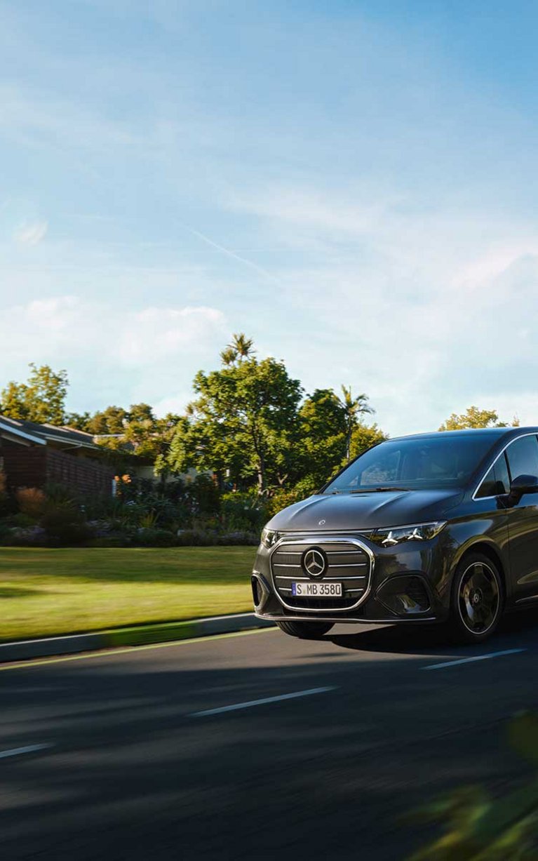 Mercedes-Benz VLE schwarz am Fahren auf der Straße mit Bäumen und Wiese im Hintergrund.