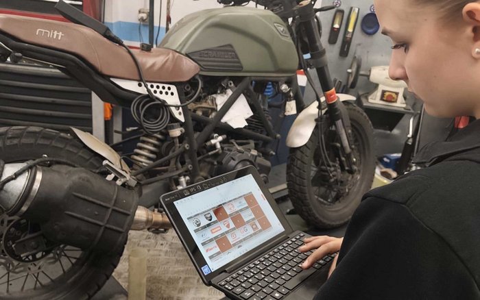 Kfz-Mechatronikerin arbeitet während ihres Erasmus+ Auslandspraktikums in Sevilla mit Laptop an einem Motorrad in der Werkstatt.