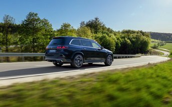 Schwarzer Mercedes-AMG GLS fährt auf einer sonnigen Landstraße durch eine grüne Landschaft.