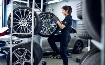 Eine Frau holt ein Reifen mit Mercedes-Benz Felgen aus dem Räderlager heraus in einer Werkstatt.