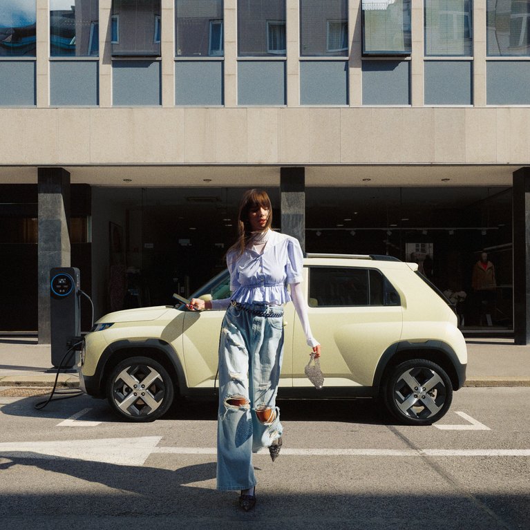 Promotionsbild für für Leasingangebote elektrischer Hyundai Fahrzeugmodelle. Eine Frau läuft vor dem Hyundai INSTER, der seitlich vor einem Gebäude geparkt ist.