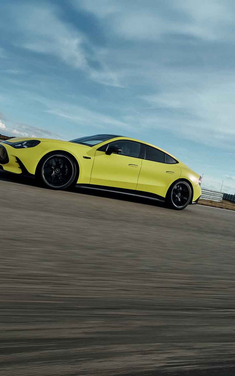 Gelber Mercedes-AMG GT 4-Türer Coupé bei dynamischer Fahrt auf einer Rennstrecke.