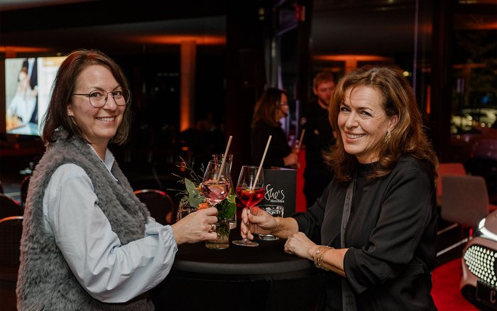 Zwei Teilnehmerinnen der She’s Mercedes Veranstaltung in Offenburg stoßen im stilvollen Ambiente des Mercedes-Benz Autohauses mit Drinks an und genießen den Abend voller Inspiration und Austausch.