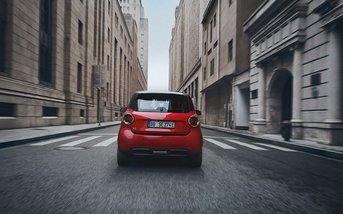 Roter vollelektrischer smart #2 Pure fährt durch eine Innenstadtstraße und zeigt sein kompaktes Design sowie seine hohe Wendigkeit im urbanen Verkehr