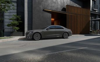 Graue Mercedes-Benz S-Klasse Limousine in Seitenansicht, geparkt vor einem modernen Gebäude mit Holz- und Betonfassade bei Tageslicht.