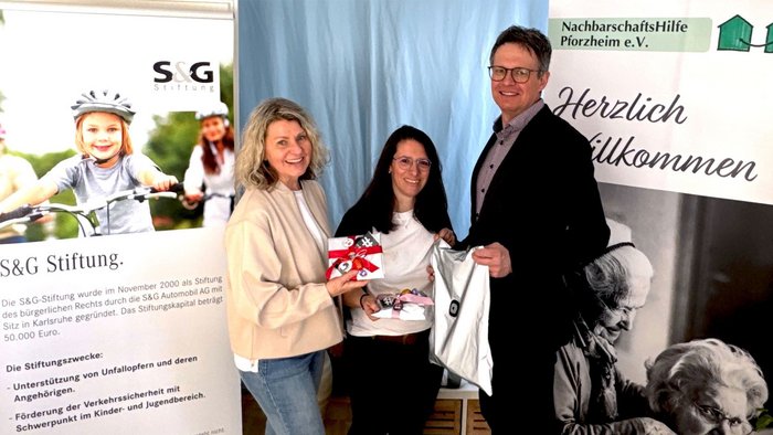2 Frauen und 1 Mann stehen vor den Roll-Ups der S&G Stiftung und der Nachbarschaftshilfe und halten reflektierende Taschen für bessere Sichtbarkeit.