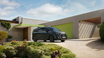 Schwarzer Mercedes-Benz VLE auf einer modernen Hauseinfahrt vor einem zeitgemäßen Wohngebäude mit grünen Akzenten, umgeben von Garten- und Landschaftselementen.