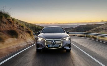 Die neue vollelektrische Mercedes-Benz C-Klasse in dynamischer Frontansicht auf einer Landstraße bei Sonnenuntergang mit markanter Lichtsignatur und modernem Mercedes-Benz Design.10,