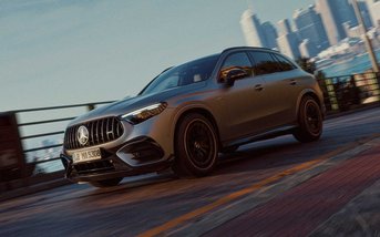 Mercedes-AMG GLC SUV fährt sportlich auf einer Straße vor moderner Stadtkulisse.