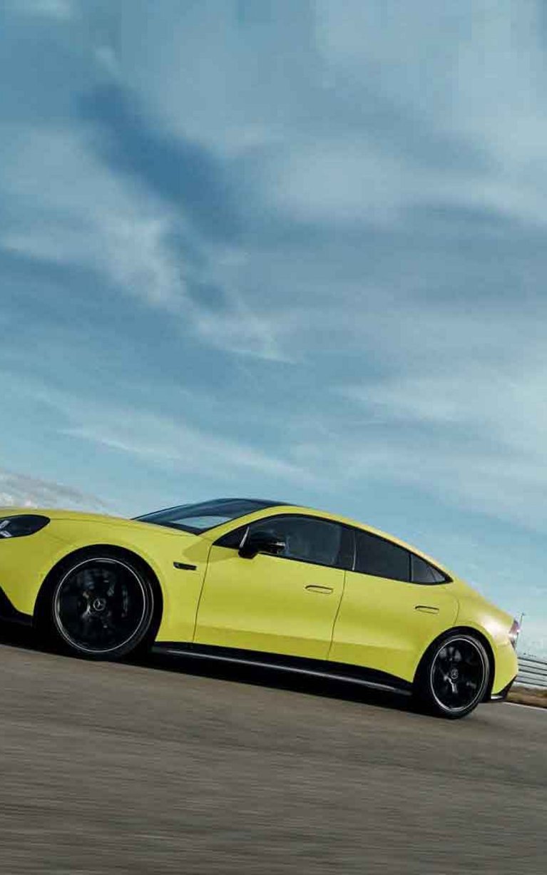 Gelber Mercedes-AMG GT 4-Türer Coupé bei dynamischer Fahrt auf einer Rennstrecke.