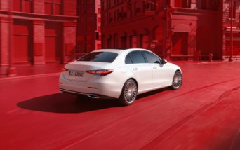 Weiße Mercedes-Benz C-Klasse Limousine fährt durch eine moderne Innenstadt mit roten Fassaden.