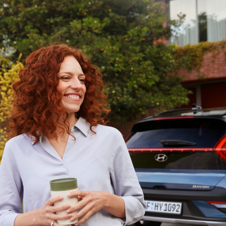 Geschäftsfrau mit Smartphone vor blauem Hyundai auf Einfahrt eines modernen Gebäudes – Symbolbild für Hyundai Angebote für Gewerbekunden bei S&G.