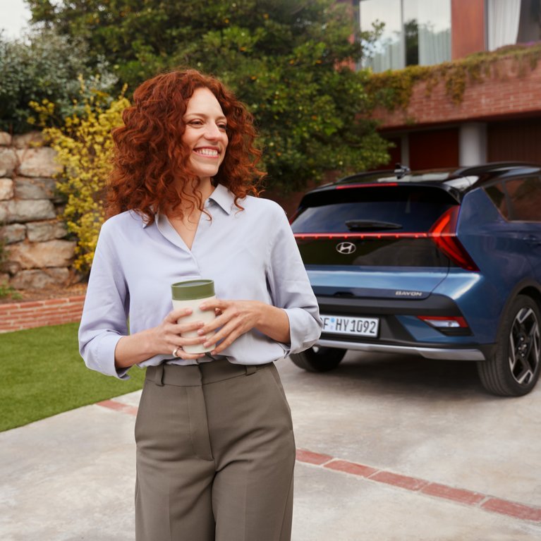 Geschäftsfrau mit Smartphone vor blauem Hyundai auf Einfahrt eines modernen Gebäudes – Symbolbild für Hyundai Angebote für Gewerbekunden bei S&G.