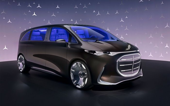 Frontansicht des Mercedes-Benz Vision V Showcars mit futuristischem Design, beleuchtetem Kühlergrill und blauer Ambientebeleuchtung im Innenraum, präsentiert auf einer Bühne mit stilisiertem Mercedes-Stern-Hintergrund.