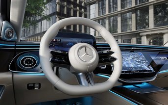 Cockpit der Mercedes-Benz S-Klasse mit modernem Lenkrad, großem digitalen Display und MBUX Infotainmentsystem, hochwertige Materialien und Ambientebeleuchtung sichtbar.