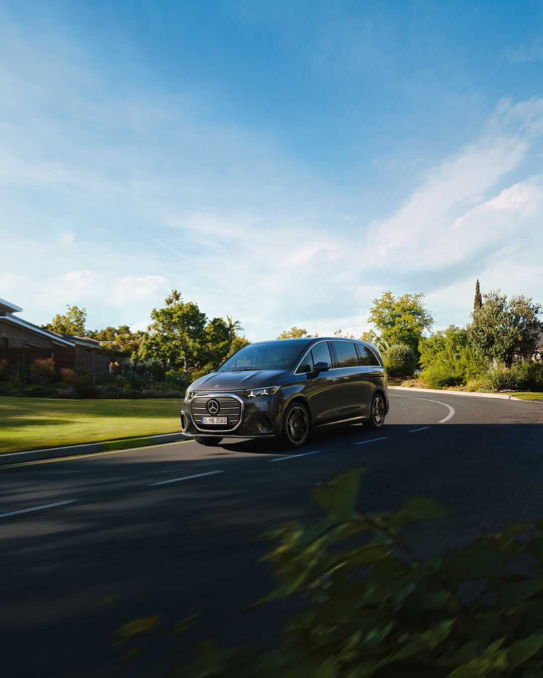 Mercedes-Benz VLE schwarz am Fahren auf der Straße mit Bäumen und Wiese im Hintergrund.